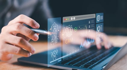 Nahaufnahme einer Person, die mit einem Stylus auf einem Laptop arbeitet, auf dessen transparentem digitalen CRM-Bildschirm Kundendaten, Analysen, Diagramme und Symbole zur Unternehmensführung angezeigt werden.  | Customer Platform-Agentur SUNZINET