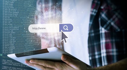 Eine Suchleiste mit einem Mauszeiger, im Hintergrund sieht man eine Person mit einem weißen Shirt und einem karierten Hemd, die ein Tablet hält. KI-Suche im Öffentlichen Dienst_SUNZINET Digital Agentur